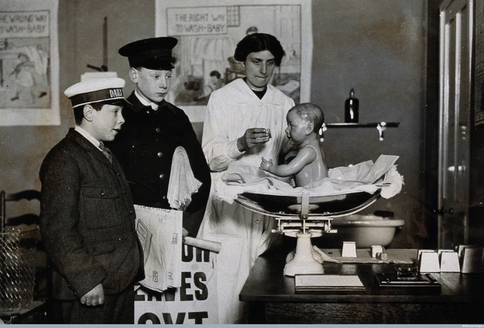 Ideal Home Exhibition, England, 1920: a rubber baby being used to demonstrate feeding methods, watched by two boys. Photograph, 1920. 1920 - Image courtesy of the Wellcome Library, London